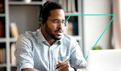 Mann mit Headset und Brille arbeitet am Laptop und hält einen Stift