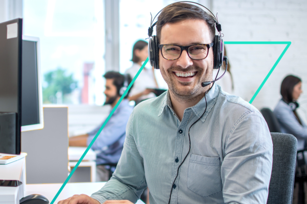 Lächelnder Mann mit Headset und Brille im Büro mit Kollegen im Hintergrund