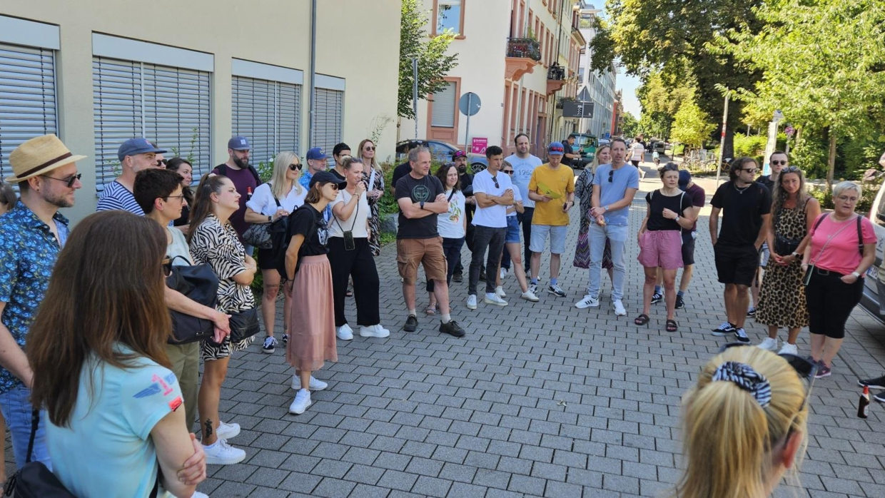 Personengruppe im Halbkreis auf gepflasterter Straße bei sonnigem Sommertag