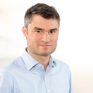 Portrait Daniel Loefler im hellblauen Hemd vor hellem Hintergrund.